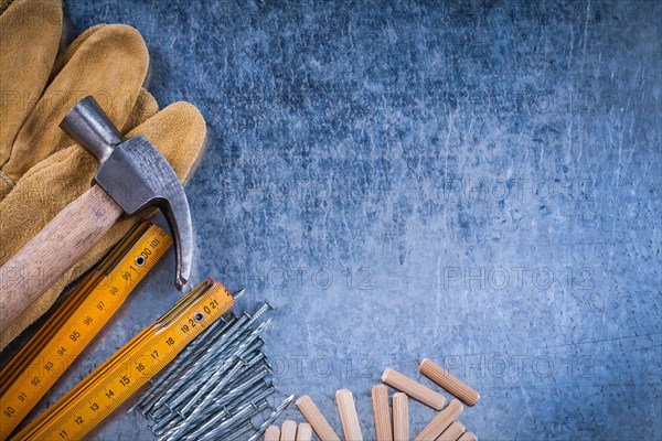 Composition of hammer safety gloves wooden meter stainless nails and dowels on scratched metallic surface construction concept