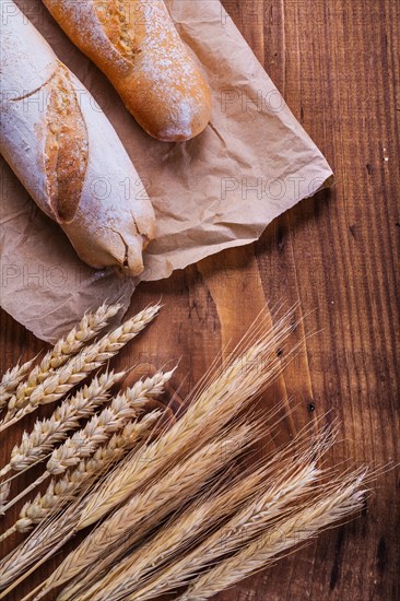 Baguettes on paper and ears of wheat old wooden board