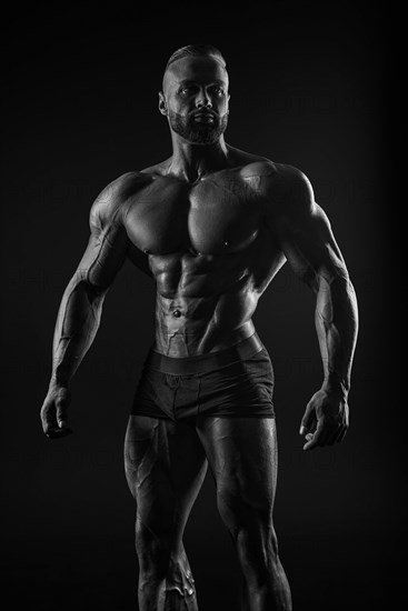 Silhouette of a strong bodybuilder. Confident young fitness athlete with a powerful body and perfect abs. Black and white photography. Dramatic light. Mixed media