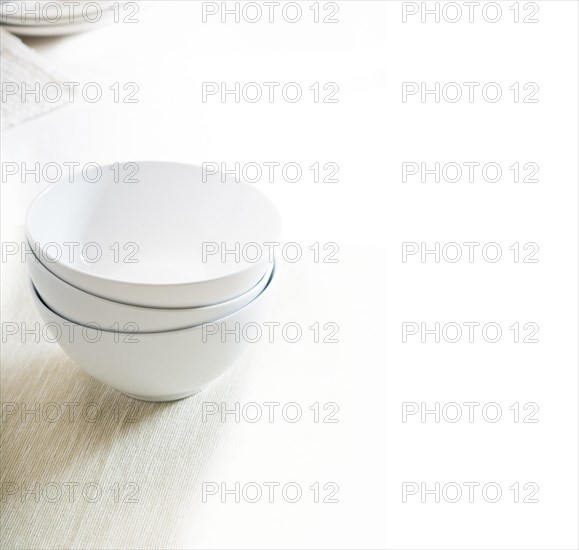 White bowls stacked over white table cloth with dishes on background