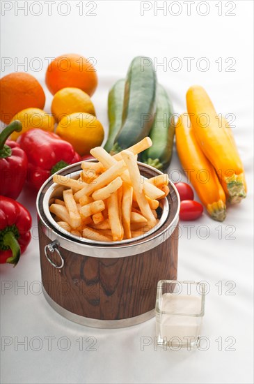 Fresh french fries on a wood bucket with white dip sauce and fresh vegetables on background