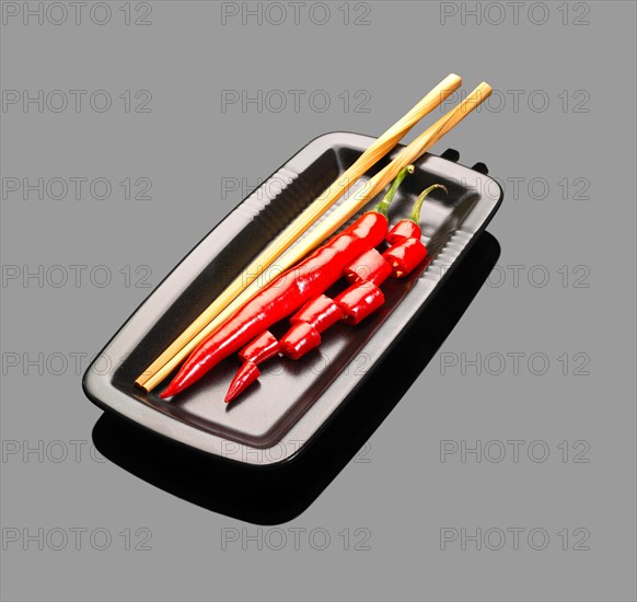 Fresh red chili peppers on a plate with chopstikcs over grey reflective surface