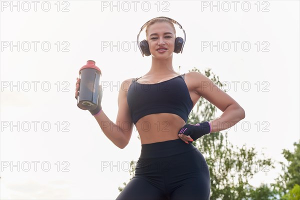 Girl posing with a sports nutrition shaker in the park. The concept of a healthy lifestyle. Sports Equipment. Fitness style advertisement. Mixed media