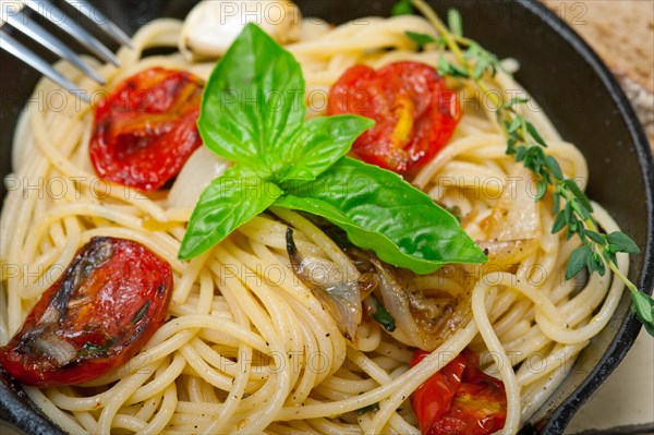 Italian spaghetti pasta with baked tomatoes basil and thyme sauce on a cast iron skillet