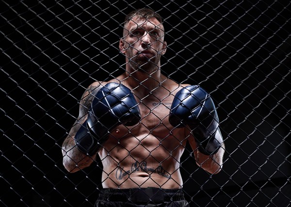 Dramatic image of a mixed martial arts fighter standing in an octagon cage. The concept of sports