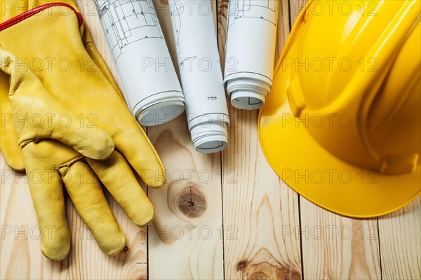 Yellow gloves blueprints and construction helmet on wood