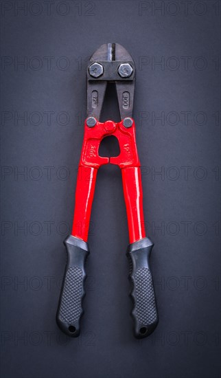 Aerial view of a red steel cutter with rubber handle on a black background