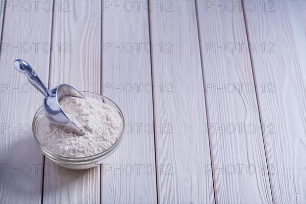 Bowl with flour and shovel on white lacquered old wooden board Food and drink concept