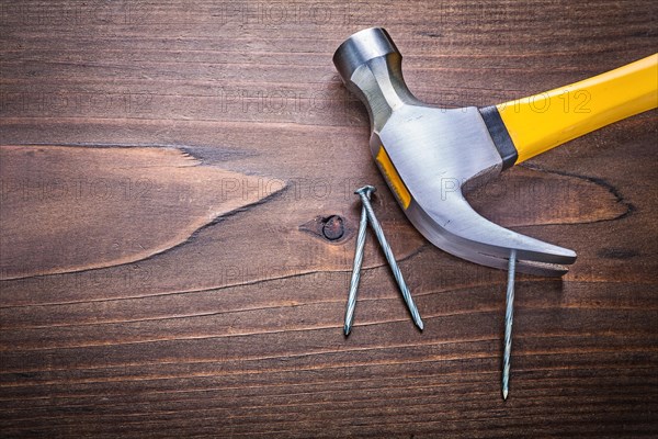 Copyspace image claw hammer with yellow handle and nails on vintage wooden board Construction concept