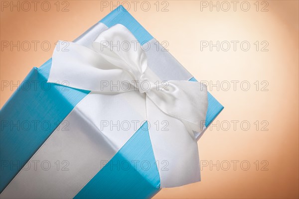 Gift box with white bow on light brown background with copy space
