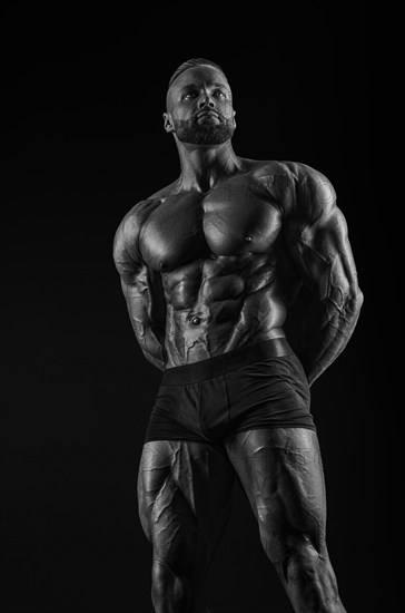 Silhouette of a strong bodybuilder. Confident young fitness athlete with a powerful body and perfect abs. Black and white photography. Dramatic light. Mixed media