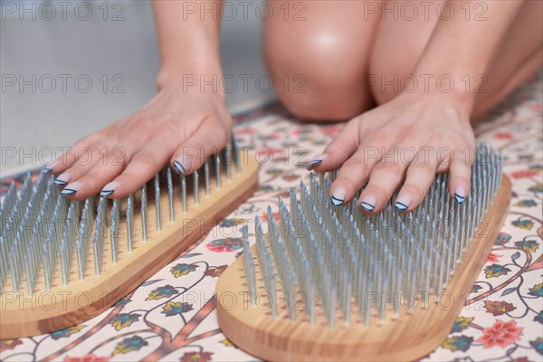 Image of a young woman in a gymnastic suit sitting on a mat in a bright studio preparing for meditation with a sadhu board. The concept of fitness