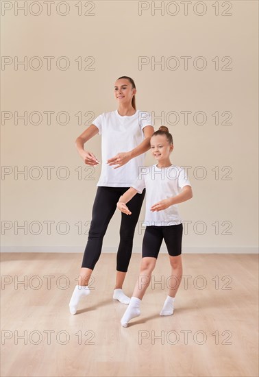 Beautiful woman teacher and a little girl perform dance movements in a bright studio. The concept of education