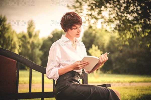 Retro image of a stylish beautiful woman sitting in a park on a bench with a book in her hands. The concept of style and fashion