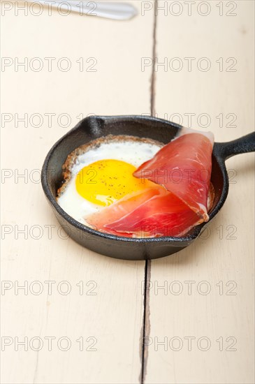 Fried egg sunny side up with Italian tyrolean speck smoked ham on a skillet