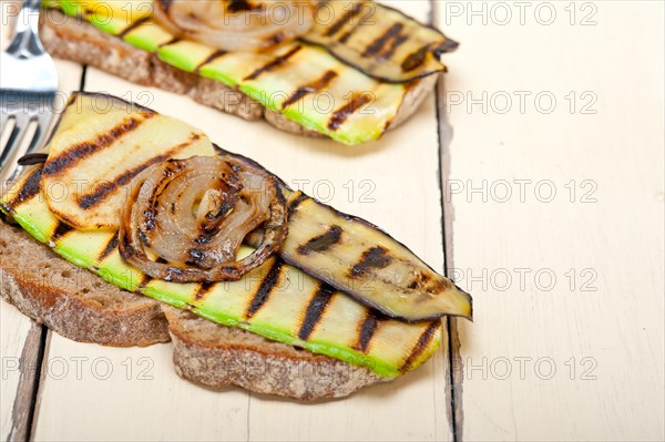 Grilled vegetables on rustic bread over wood table