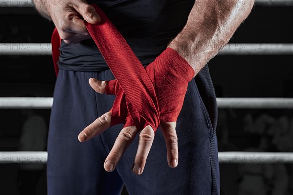 Red bandages on the hands of a kickboxer against the background of the ropes of the ring. The concept of mixed martial arts. MMA