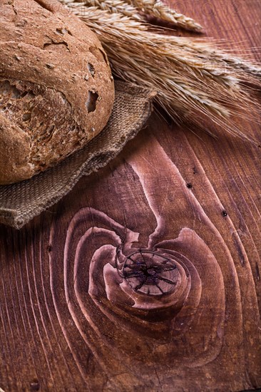 Loaf of bread and ears of wheat on an old wooden board