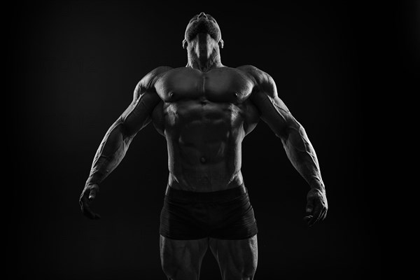 Silhouette of a strong bodybuilder. Confident young fitness athlete with a powerful body and perfect abs. Black and white photography. Dramatic light. Mixed media