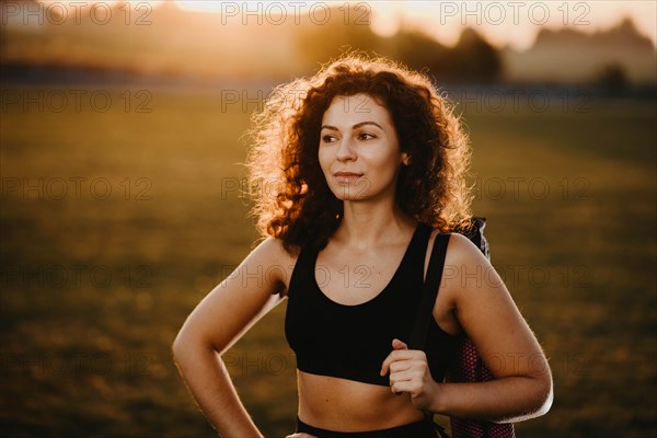 Curly girl runner with a yoga mat stands at sunset on the lawn