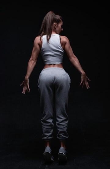 Athletic fitness woman posing in the studio on a dark background. Photo of an attractive woman in fashionable sportswear. Sports and healthy lifestyle. Mixed media