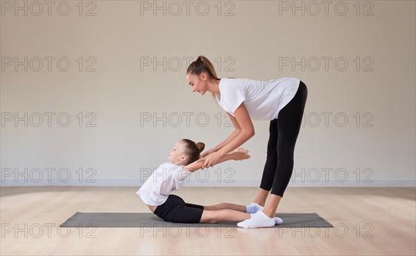 Beautiful female teacher helps a little girl stretch in a gymnastics class. The concept of education