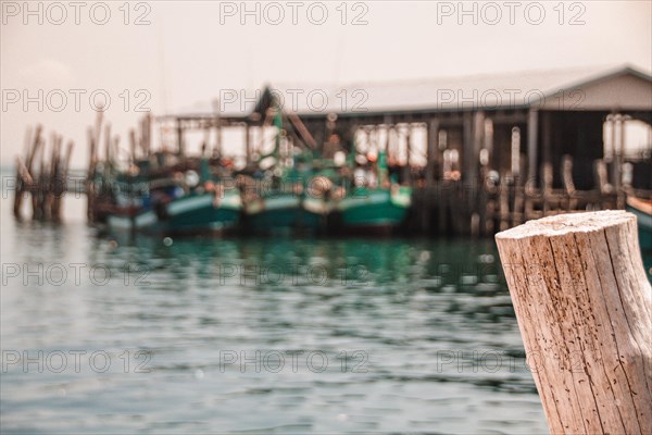 Close-up of a wooden post with moored boats at a pier in soft focus at the background. Koh Sdach Island