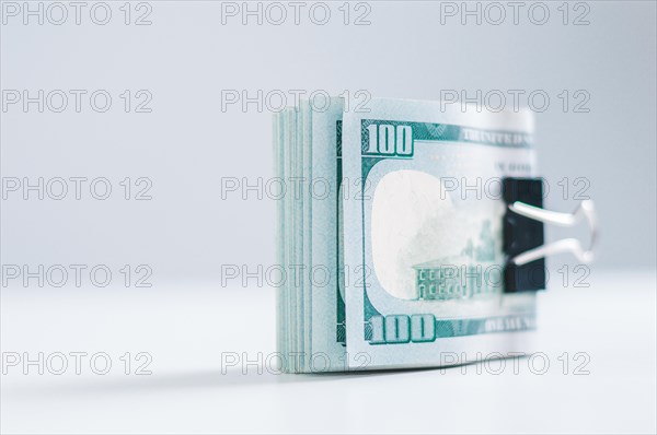 Pack of hundred-dollar bills lies on a white table fastened with a paperclip. The concept of savings during the crisis.