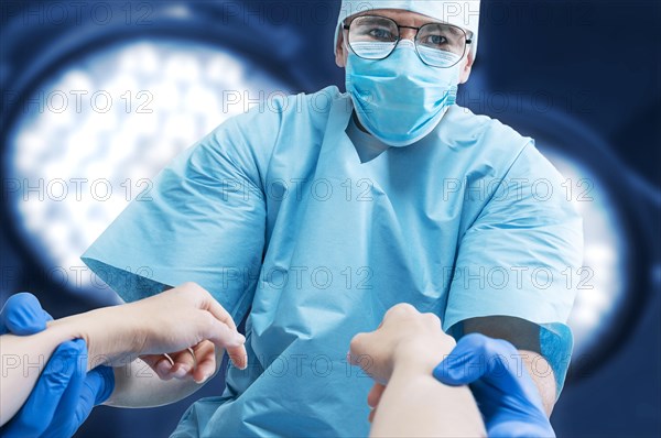 Portrait of a doctor in a mask on a background of surgical lamps. He holds the patient's hands. Medicine concept.