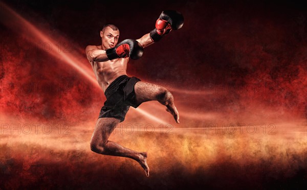 Professional kickboxer jumps with his knee extended. Fiery arena. Mixed martial arts. Sports concept