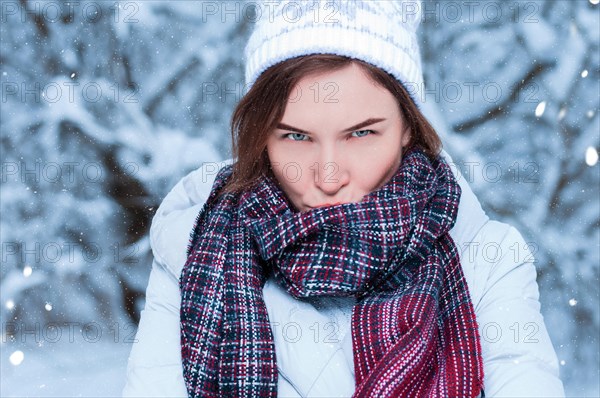 Beautiful girl with a displeased expression on the background of snowy trees. Snowball game. Christmas holidays concept.