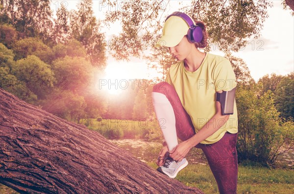 Portrait of a beautiful girl running in a sunny park in headphones with a smartphone. Music apps concept.