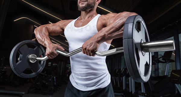 Handsome young man working out with a barbell in the gym. Shoulder pumping. Barbell pull to the chin. Fitness and bodybuilding concept