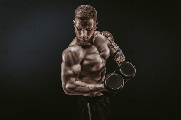 Young muscular guy pumping biceps with dumbbells. Concentrated flexion. Fitness and nutrition concept.