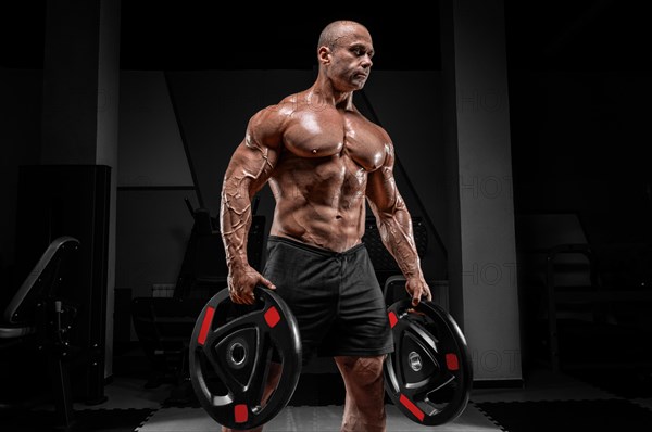 Muscular man stands in a gym with barbell discs. Bodybuilding and powerlifting concept.