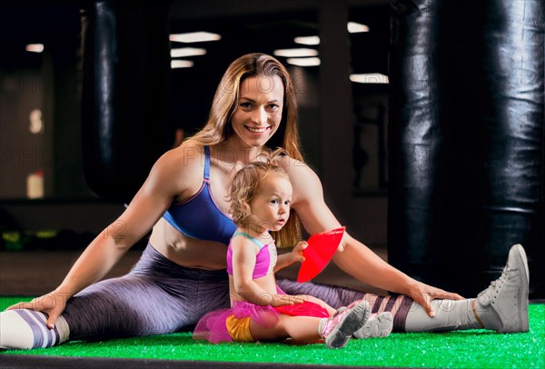 Charming sports mom trains in the gym with her little daughter and a French bulldog.