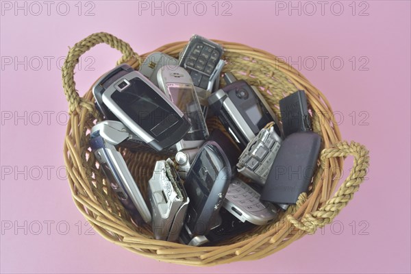 A basket filled with a variety of old cell phones on a pink background