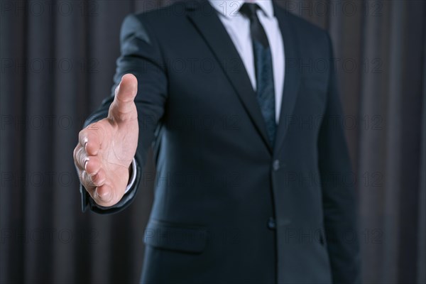 Image of a stylish man in a suit holding out his hand for a handshake. Business concept.