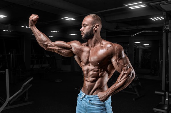 Muscular man in jeans poses in the gym. Sports