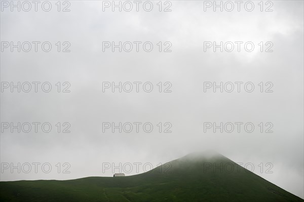 Grassy mountain peak with mountain hut in the fog