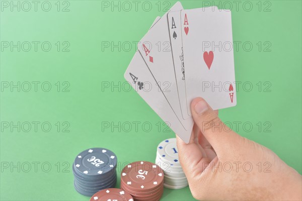 Four aces in a hand with various denomination poker chips on a green felt background