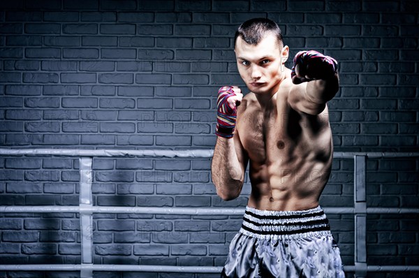 Thai boxer stands in the ring and punches in front of him. The concept of sports