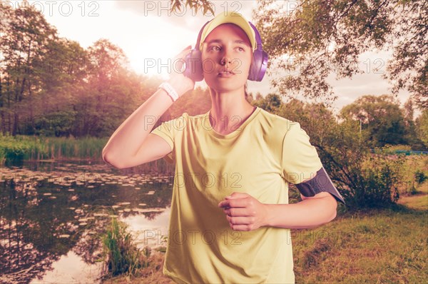 Portrait of a beautiful girl running in a sunny park in headphones with a smartphone. Music apps concept.