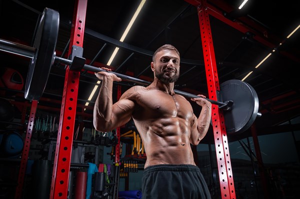 Muscular man posing in the gym with a barbell. Fitness concept.