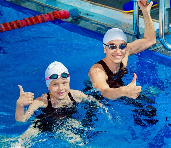 Charming coach with his student swimming in the pool and smiling