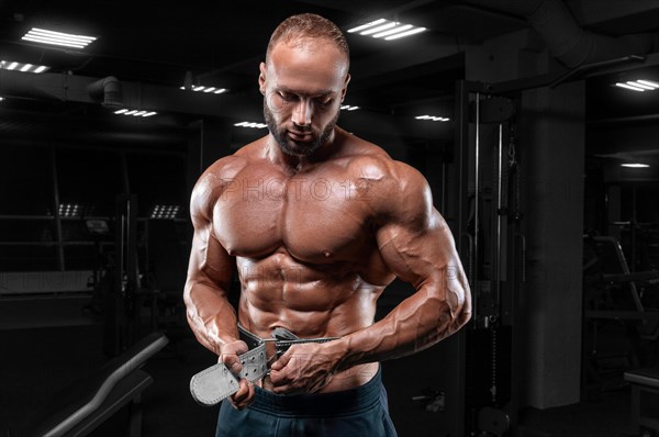 The athlete poses in the gym with an athletic belt. Fitness