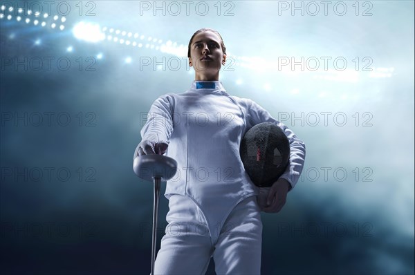 Charming girl dressed as a fencer posing with a mask and a sword. The concept of fencing.