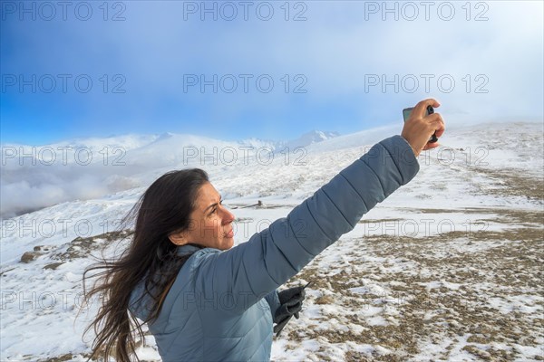 Latina woman taking a selfie with a smartphone while enjoying a winter day in sierra nevada