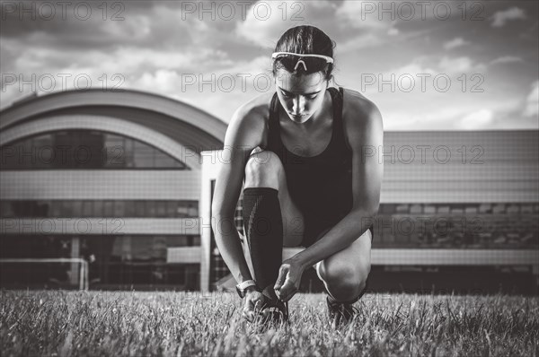 Portrait of a young runner who laces her boots at a football stadium. Sports concept.