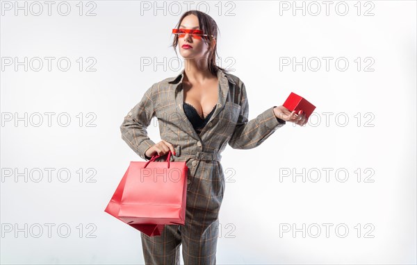 Charming brunette in glasses posing in the studio with red bags and a box for jewelry. White background. Shopping concept.